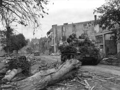 Un M5A1 estadounidense camuflado con ramas pasando a través de las calles de pueblo normando de Coutances durante la Batalla de Normandía.